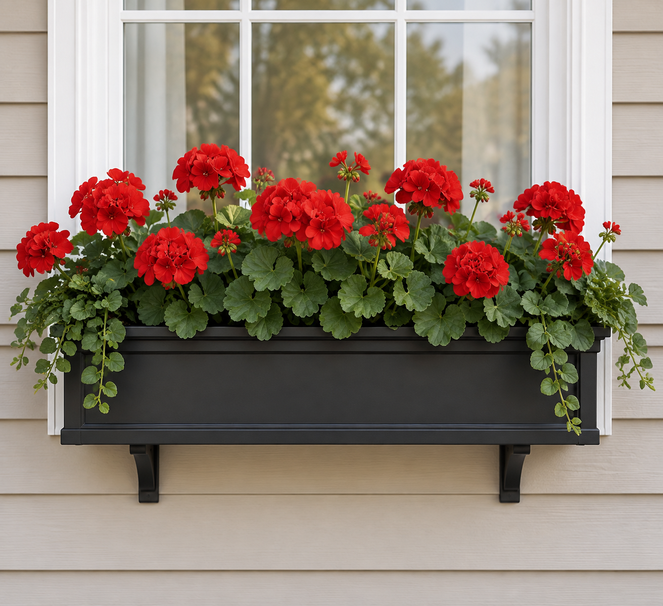 An artificial red geranium window box mounted under a white-trimmed window