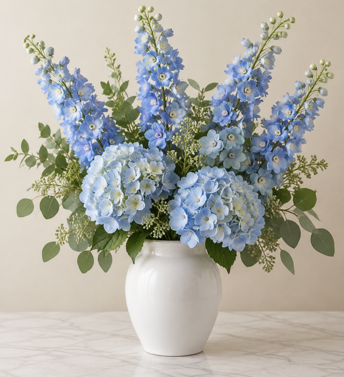 Blue artificial delphinium and hydrangea flowers arranged in a white vase