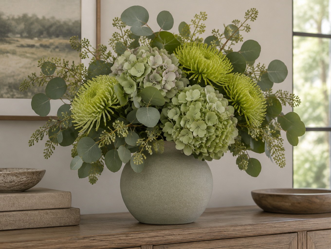 Tonal green flower arrangement of sage hydrangeas, chartreuse spider mums and eucalyptus in a matte ceramic vase on a wood console