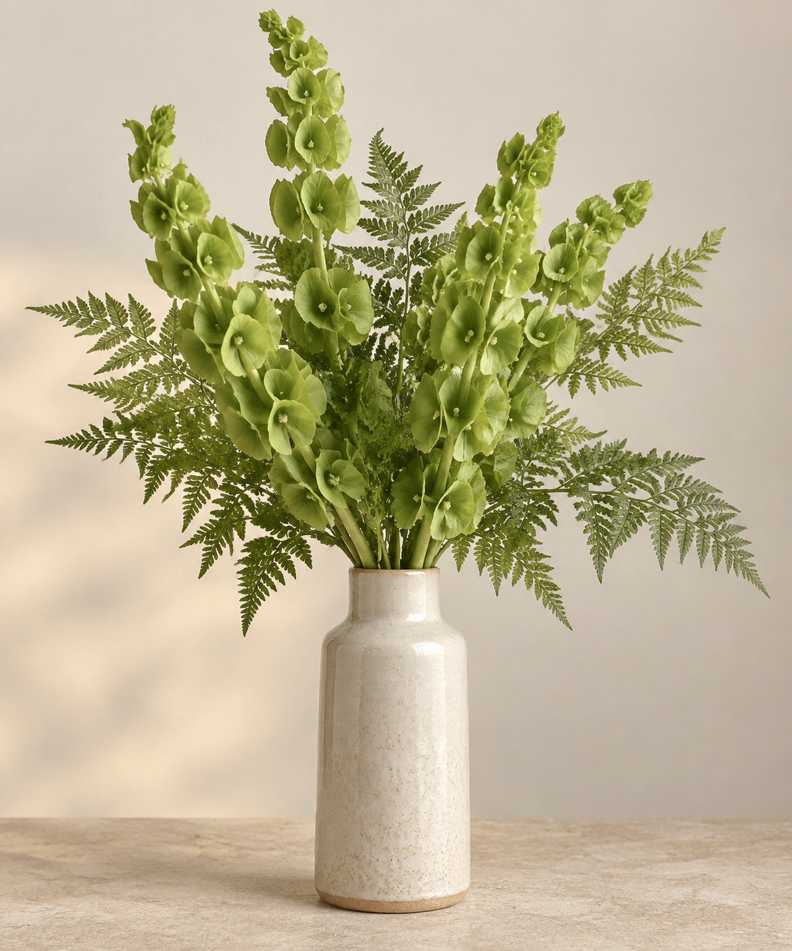 Green artificial bells of Ireland and ferns arranged in a ceramic bottle vase