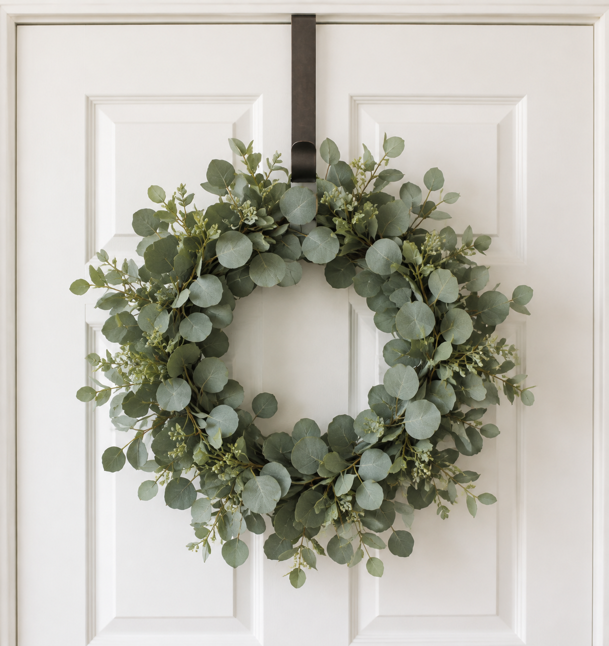 Eucalyptus wreath hanging from a black metal over-the-door hook on a white paneled door