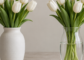 A ceramic vase and a clear glass vase side by side on a table, each holding the same white artificial tulips at the same height